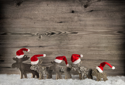 Geschnitze Elche oder Hirsche aus Holz mit Weihnachtsm&uuml;tzen auf Holz Hintergrund.