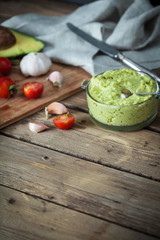 Guacamole on wooden table surrounded by its ingredients..