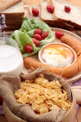 Breakfast with eggs, sausage, bread, salad vegetables and milk.