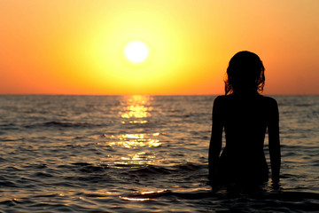 silhouette of a girl in a bathing suit in the sea at sunrise