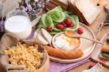 Breakfast with eggs, sausage, bread, salad vegetables and milk.