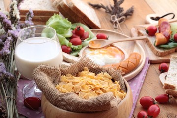 Breakfast with eggs, sausage, bread, salad vegetables and milk.