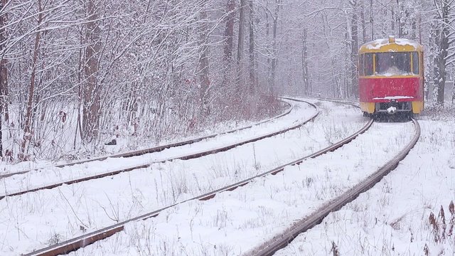 Old tram goes through the snowy woods. Railway in the winter.