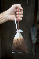 Obraz premium Hand holding fresh traditional Thai style iced coffee with condensed milk served in a handy plastic bag with a straw