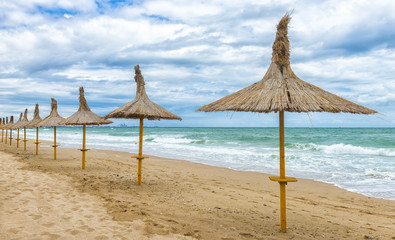 Beautifull empty beach in a windy day with straw umbrellas