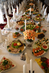 Long spread served festively decorated table with rose bouquets fabric napkins white candles and different snacks with nobody, vertical picture