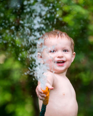 Child, Boy or kid plays with water hose outdoors during summer o