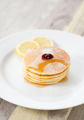 Stack of homemade pancakes with honey and lemon on plate