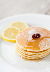 Stack of homemade pancakes with honey and lemon on plate