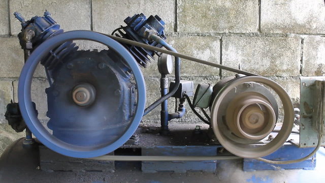 Air compressor is running. Dark blue air pump and motor is running on concrete block background in factory.
