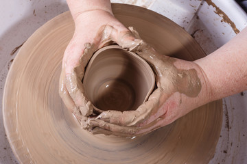 Hands working with clay on potter's wheel.