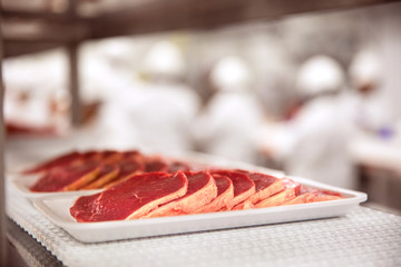 Cuts of meat portioned on styrofoam on a conveyer belt at a processing plant
