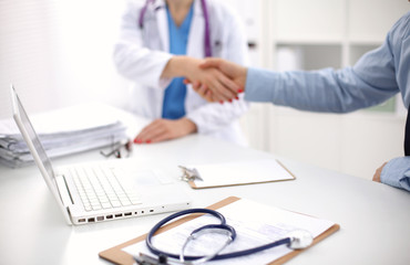 Fototapeta premium Attractive female doctor shaking a patient's hands in her office