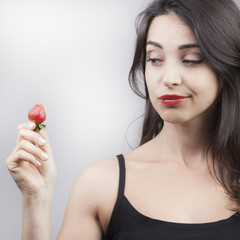 Giovane e bella ragazza guarda una fragola con desiderio prima di mangiarla
