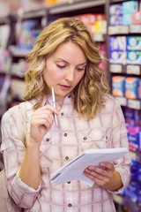 Smiling pretty blonde woman writing on her notepad and thinking 