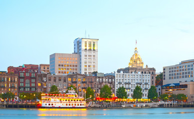 Obraz premium Savannah Georgia USA, skyline of historic downtown at sunset with illuminated buildings and steam boats