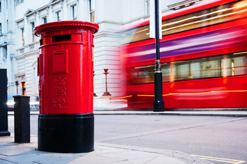 Naklejka premium Traditional red mail letter box and red bus in motion in London, the UK.