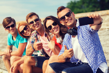 group of smiling friends with smartphone outdoors