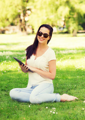smiling young girl with tablet pc sitting on grass