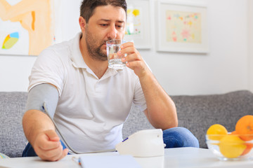 Man measuring his blood pressure and drinking a glass of water