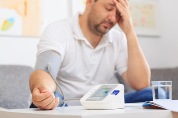 Man measuring his blood pressure having a headache. Blurred background