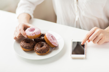 close up of hands with smart phone and donuts