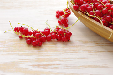 Fresh berries of red currant in a wooden bowl on a light wooden surface