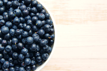 Fresh bilberry in a white ceramic bowl on a wooden surface