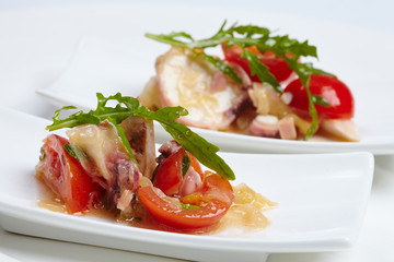 Swedish table appetizers: tomatoes, cheese, arugula, octopus, on