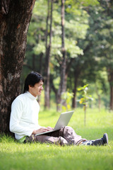 Naklejka na ściany i meble Young man using his laptop on the grass