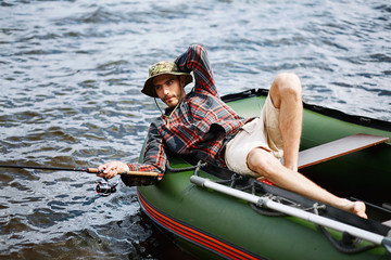 Obraz premium young happy man on vacation lying in the boat smile and fishing