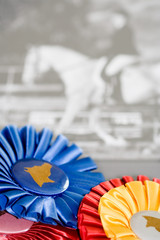 Naklejka premium Blue Ribbon Horse – Blue, yellow and red ribbons in foreground, with horse and rider in background.