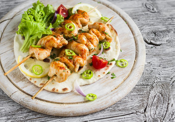 chicken kebabs and fresh vegetable salad on a homemade tortilla on a light wooden background