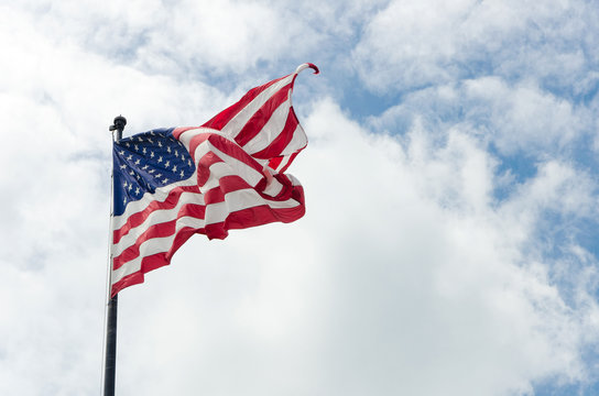 US American flag waving in the wind with beautiful blue cloudy sky in background