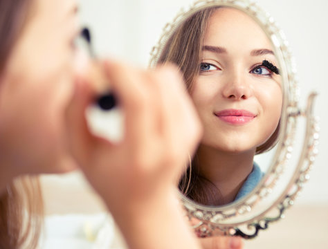 Beauty model teenage girl looking in the mirror and applying mascara