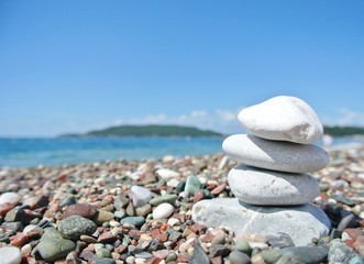 Stack of white stones balancing on the pebbly beach, on a sunny day, with sea in the background. Concept of balance, peace, harmony, well-being, and zen.