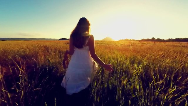 Attractive young woman walking in a grassy field at sunset