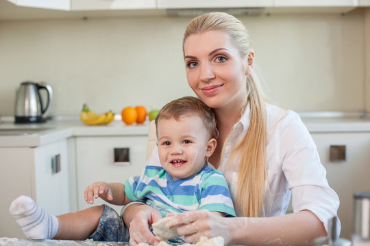 Beautiful housewife is cooking with her kid in kitchen