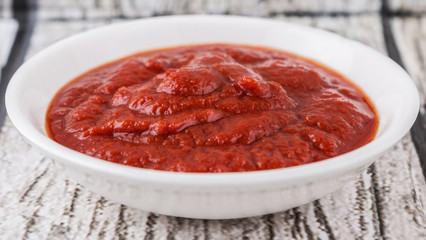 Fresh pureed tomato in white bowl over rustic wooden background
