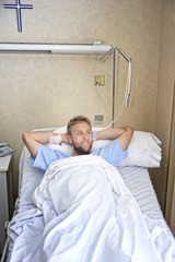 young American man lying in bed at hospital room sick but happy