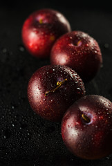 Low key shot of Plums on a black, smooth and wet surface
