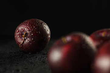 Low key shot of Plums on a black, smooth and wet surface