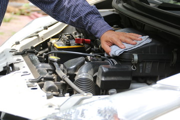 Man is cleaning his car engine with a rag.
