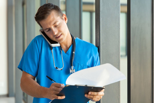 doctor writing on clipboard while talking on cell phone