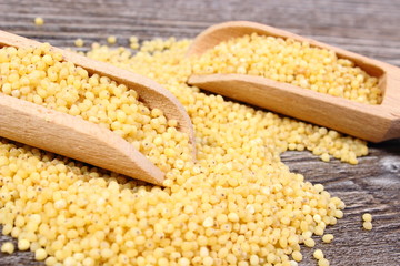 Heap of millet groats with spoon on wooden background