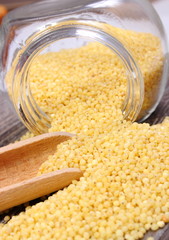 Millet groats spilling out of glass jar. Wooden background