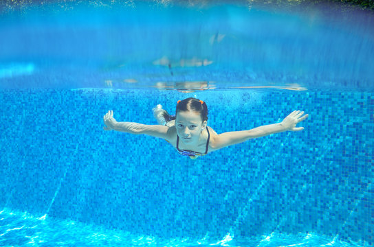 Happy girl swims in pool underwater, active kid swimming, playing and having fun
