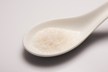 Pile of sugar in white ceramic spoon on white background