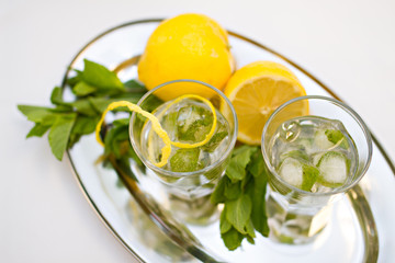 Two cocktail glasses and mint with lemons on tray