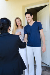 happy young couple with a real estate agent getting keys in front of their new house